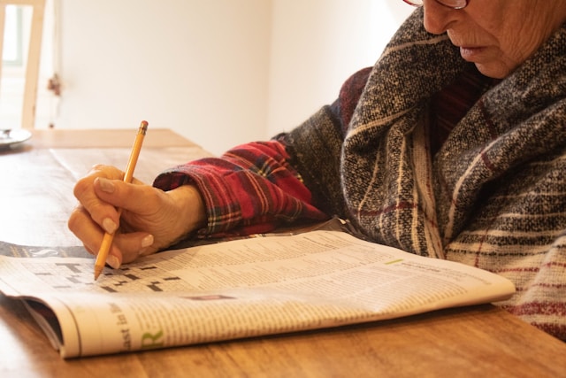 elderly woman doing a cross word at a table