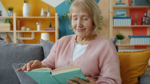 senior woman reading with a smile on her face in a quiet lounge