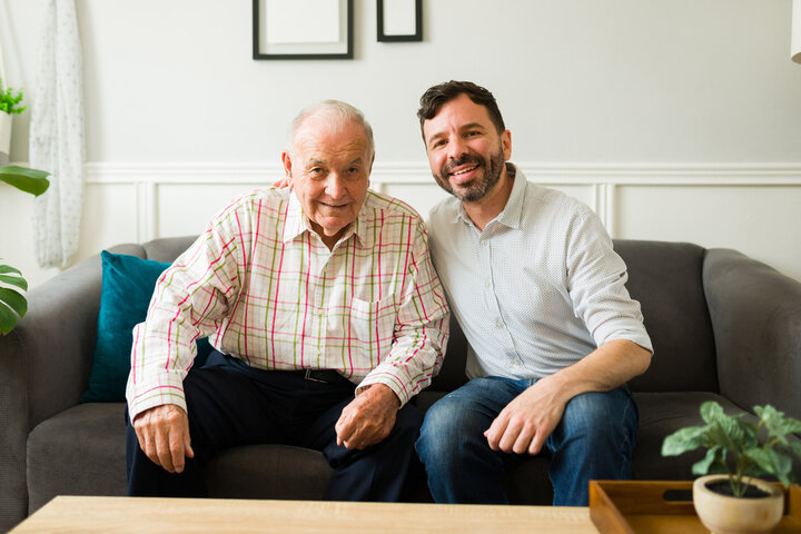 son and father in a care home smiling on the sofa