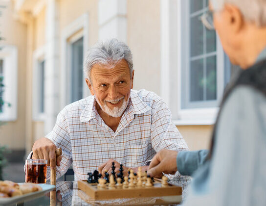 older man playing chess in the garden of a care home with another resident