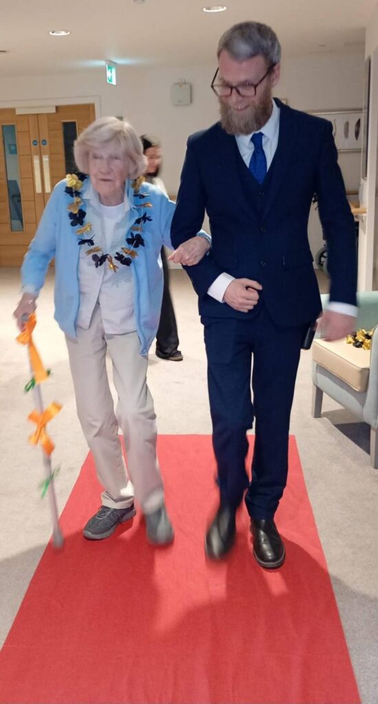 staff walking with resident down the red carpet